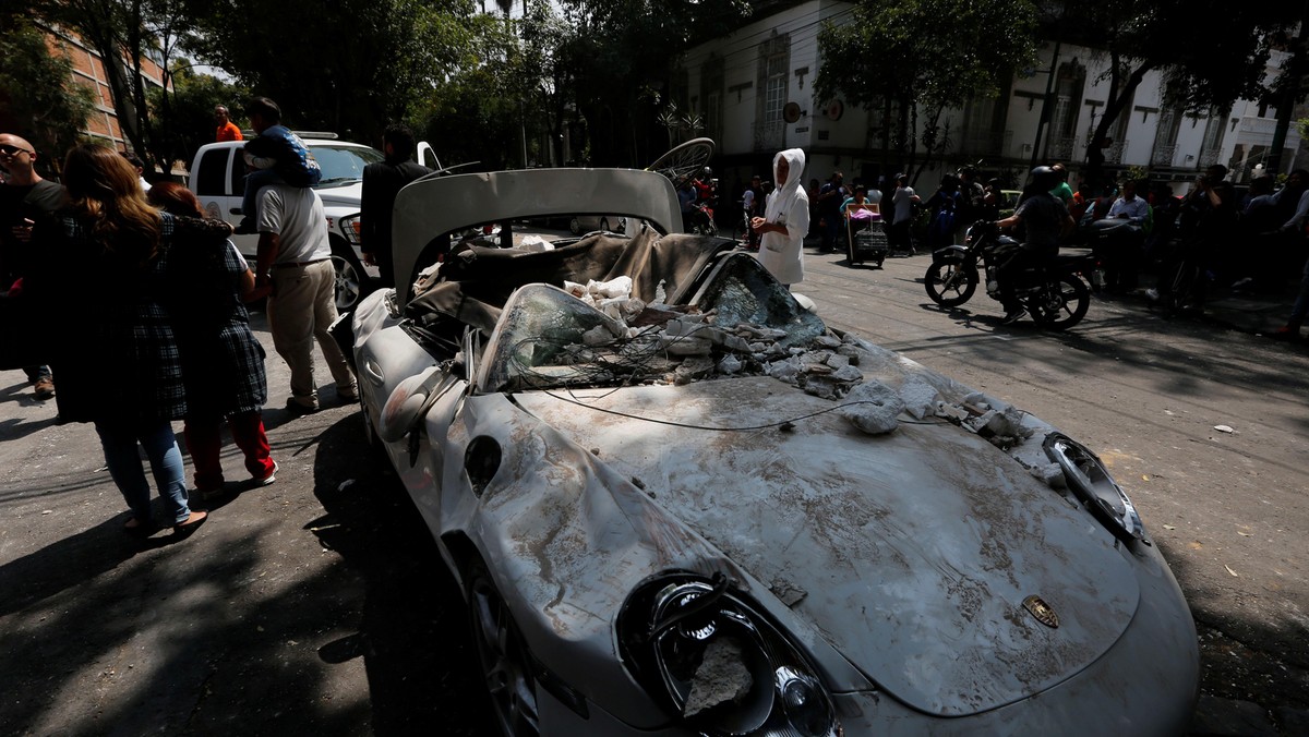 People are seen next to a damaged car after an earthquake in Mexico City