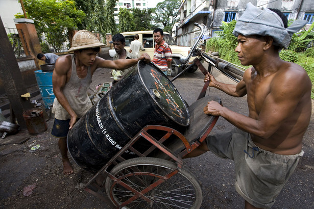 Robotnicy transportują baryłkę ropy naftowej na czarnorynkowym straganie w Yangon w Birmie.