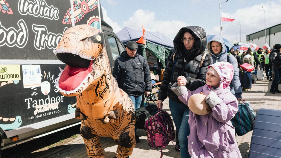 Wzdłuż alejki chodzi dinozaur i zaczepia przechodzących