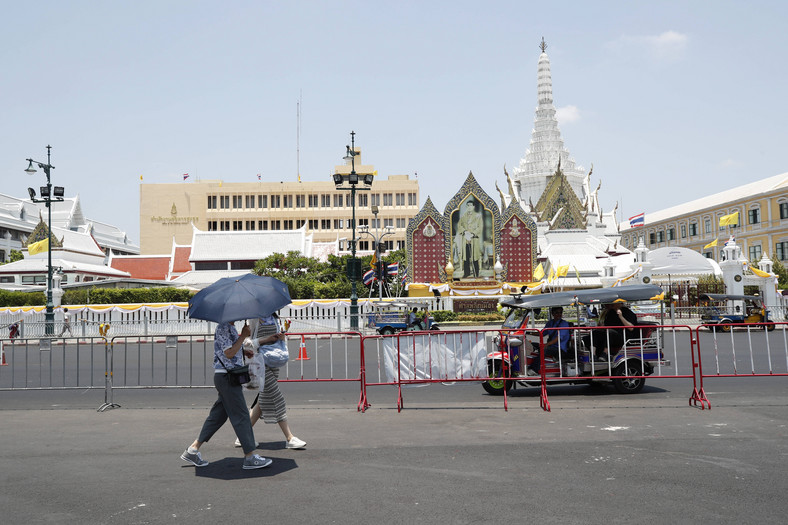 Turyści używają parasoli, aby chronić się przed promieniami słonecznymi podczas upałów w Bangkoku