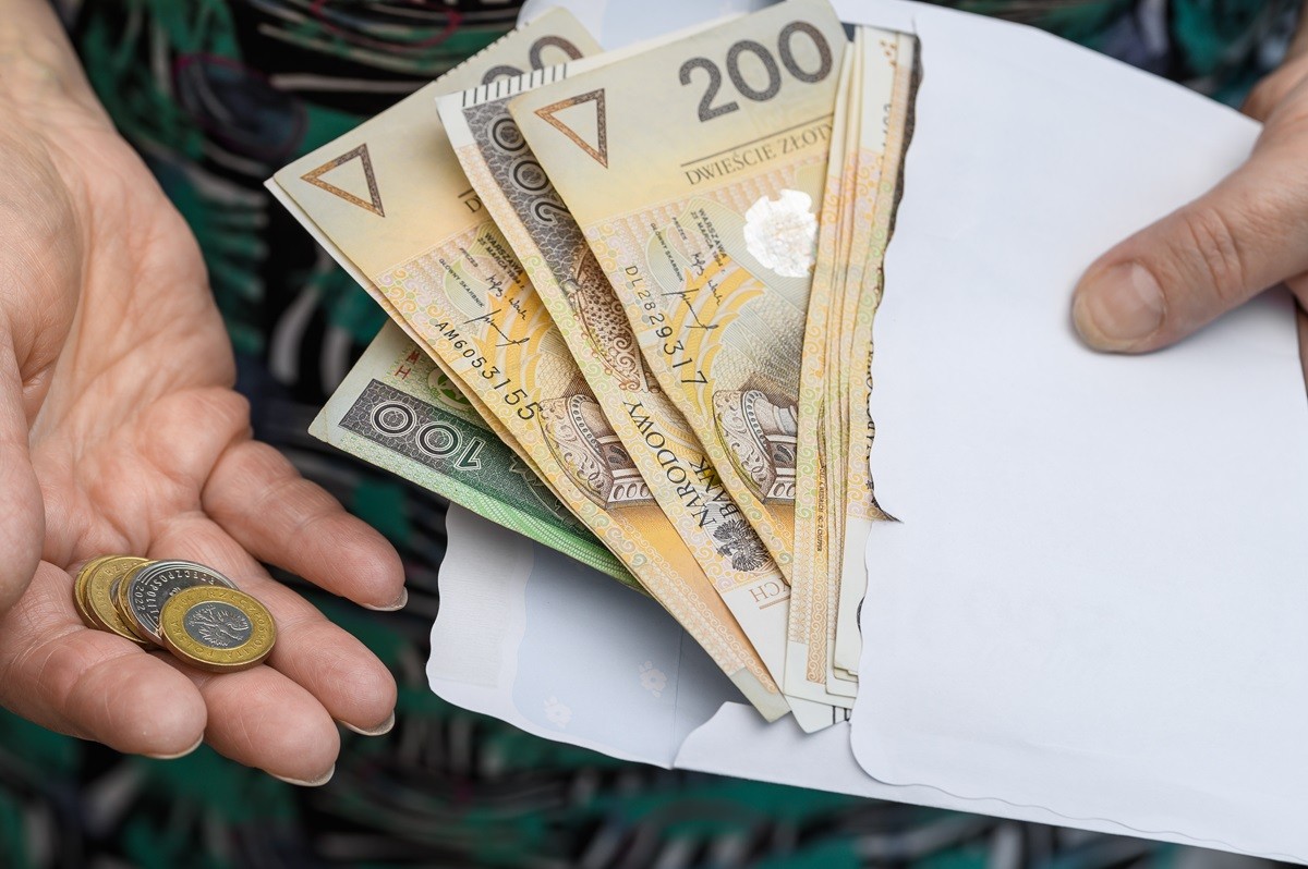 Kobieta trzymająca w jednej dłoni kopertę z banknotami 200 i 100 zł, a w drugiej kilka 2 zł