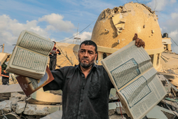 A man holds books of the Quran in front of a mosque destroyed by Israeli airstrikes.