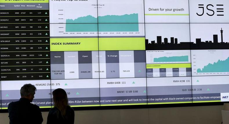 People chat in front of an electronic board displaying movements in major indices at the Johannesburg Stock Exchange building in Sandton Johannesburg July 9, 2015.  REUTERS/Siphiwe Sibeko