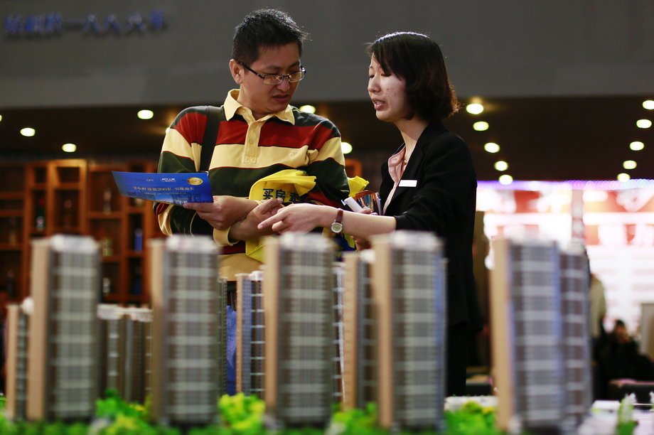 A salesperson (R) talks to a customer behind models of a residential compound at a real estate exhibition in Wuxi, Jiangsu province May 18, 2013.
