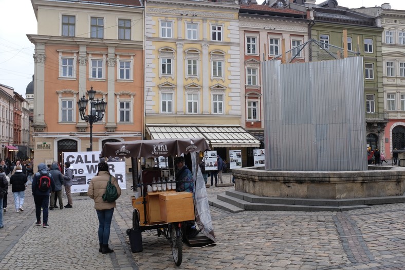 Na rynku we Lwowie można kupić kawę ze specjalnego wózka. Tuż obok ślad wojny - zabytkowa rzeźba osłonięta przed atakiem