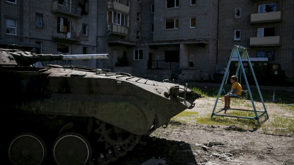 Boy sits on a swing near his building, which was damaged during fighting between the Ukrainian army and pro-Russian separatists, as an APC of the Ukrainian armed forces is seen nearby in Avdeyevka near Donetsk