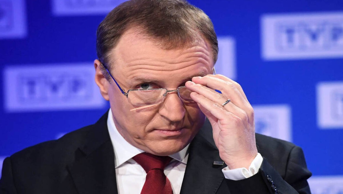 Jacek Kurski były prezes TVP spogląda na rozmówcę, trzymając okulary w dłoni