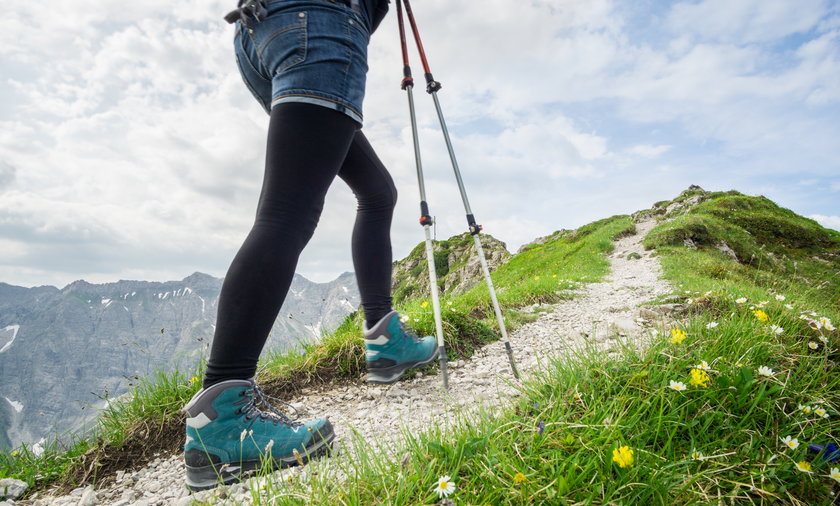 Woman running on narrow mountain trail with hiking poles.