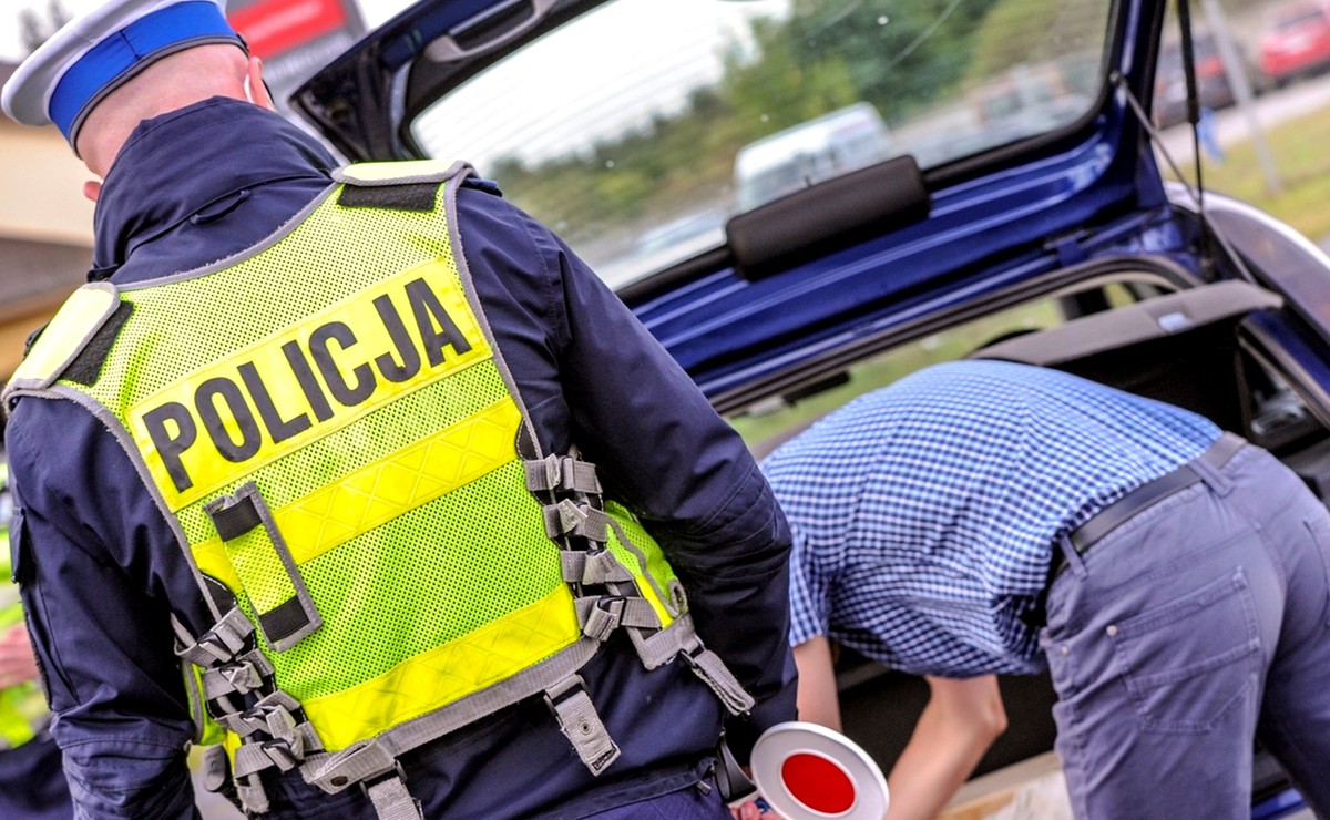 Kontrola drogowa policji, policjant sprawdza bagażnik samochodu osobowego