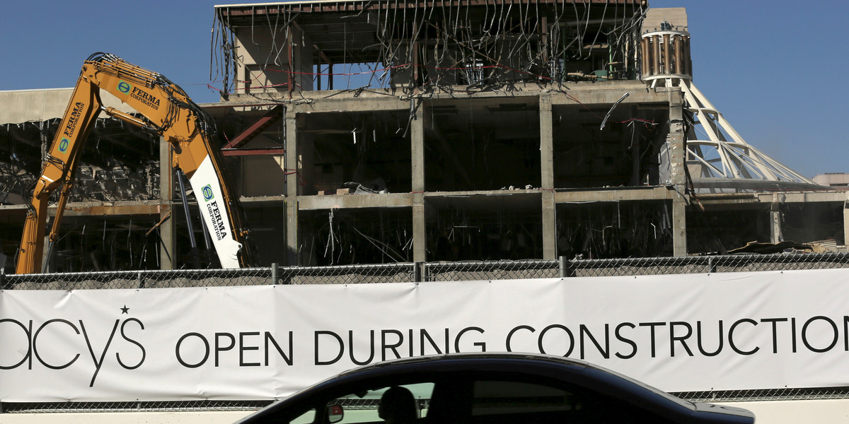A sign is seen on protective fencing as workers begin demolition on a former retail mall