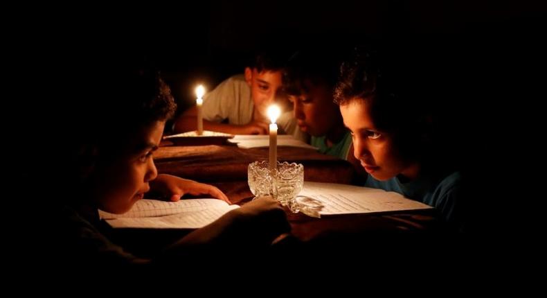 A picture taken on June 13, 2017 shows Palestinian children at home reading books by candle light due to electricity shortages in Gaza City