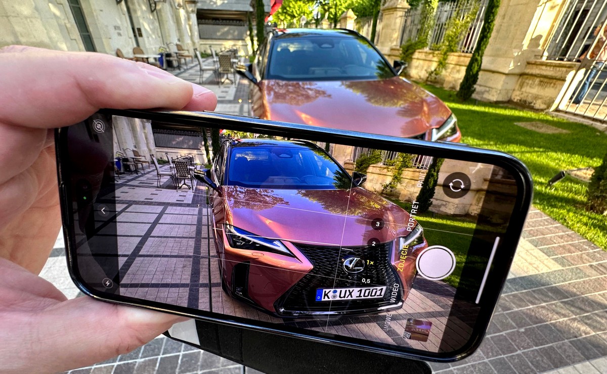 Osoba trzymająca smartfon i robiąca zdjęcie samochodu Lexus UX na parkingu, kontrola abonamentu RTV w aucie, dokumentowanie radia w samochodzie przez szybę