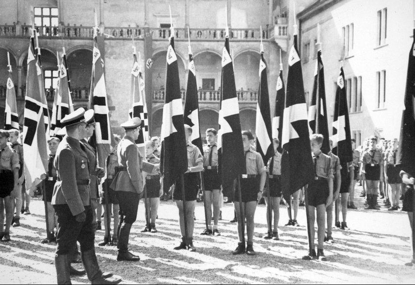 Arthur Axmann (pierwszy z prawej), Hans Frank (drugi z lewej) i Forschle przed pocztami sztandarowymi Hitlerjugend na dziedzińcu Zamku Królewskiego w Krakowie.