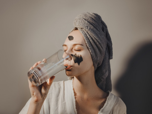 Kobieta z maseczką na twarzy pije napój kolagenowy