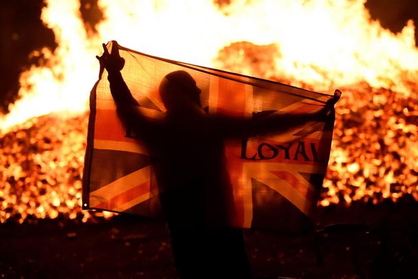 A man holds a Union flag in front of a bonfire in the Sandy Row area after it is lit by petrol bombs