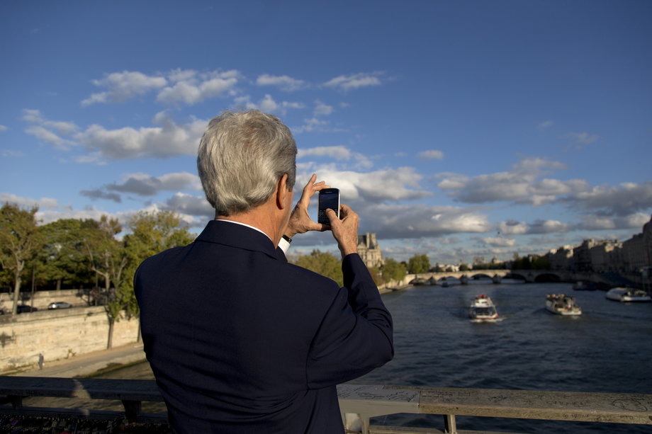 FRANCE: Kerry pauses to take a photograph of the River Seine from the Pont des Arts pedestrian bridge on his way to meet with French Foreign Minister Laurent Fabius at the Quai d'Orsay in Paris, October 13, 2014.