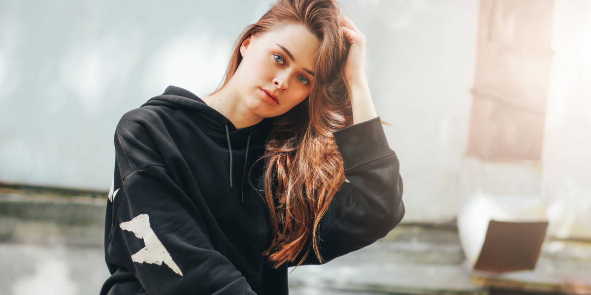 Candid portrait of young beautiful long hair unhappy girl fashion model hipster in black hoodie on w