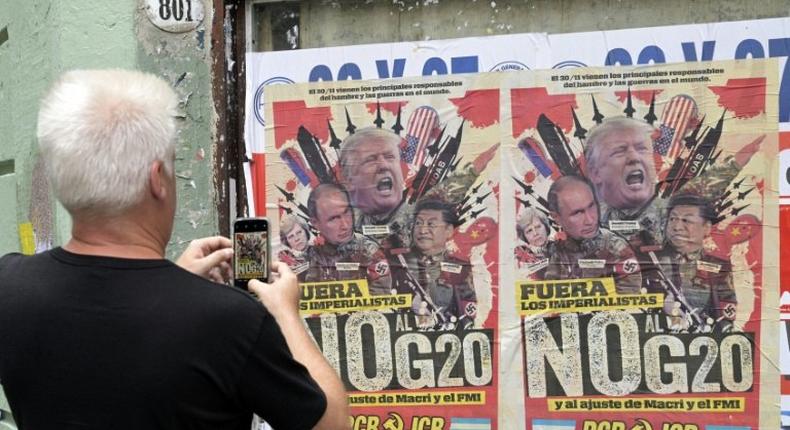A passerby takes a picture of a poster protesting the G20 summit in Buenos Aires