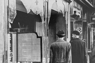 Germans pass by the smashed windows of a Jewish-owned shop. The aftermath of Kristallnacht (Night of