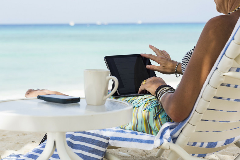 Kobieta na plaży w Kajmanach wykonująca swoją pracę zdalnie za pomocą laptopa