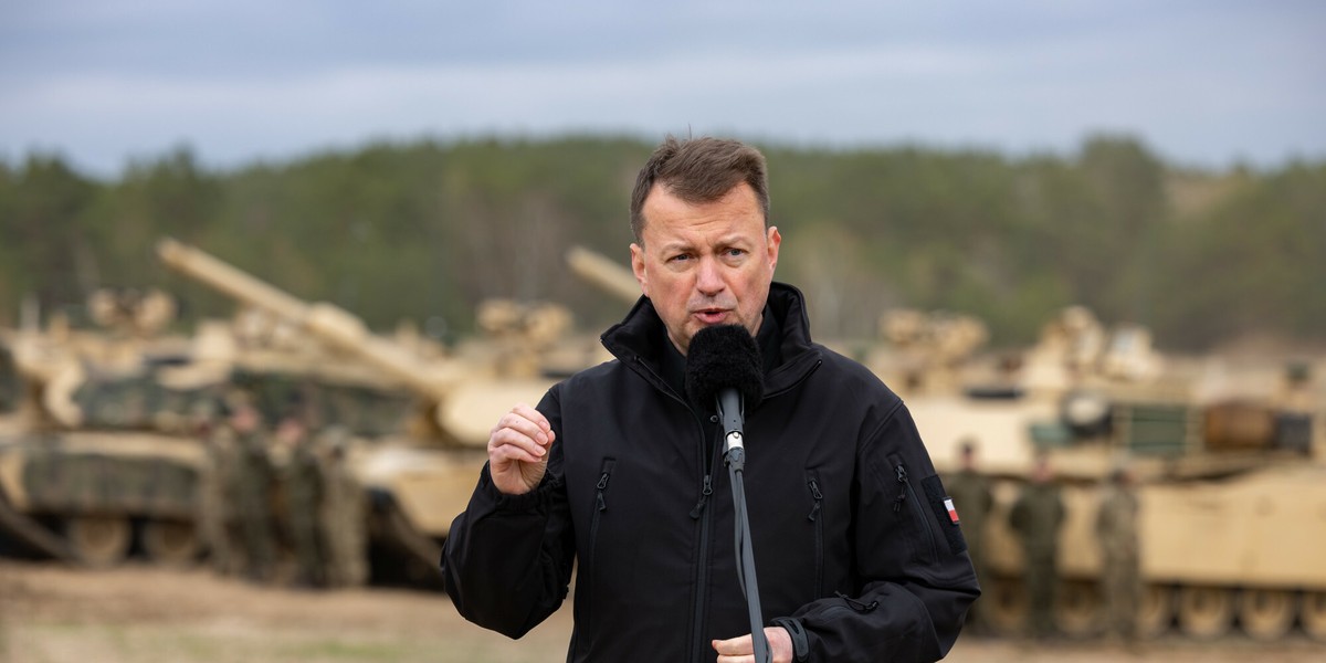 Minister Mariusz Błaszczak na tle amerykańskich czołgów na poligonie w Drawsku Pomorskim.