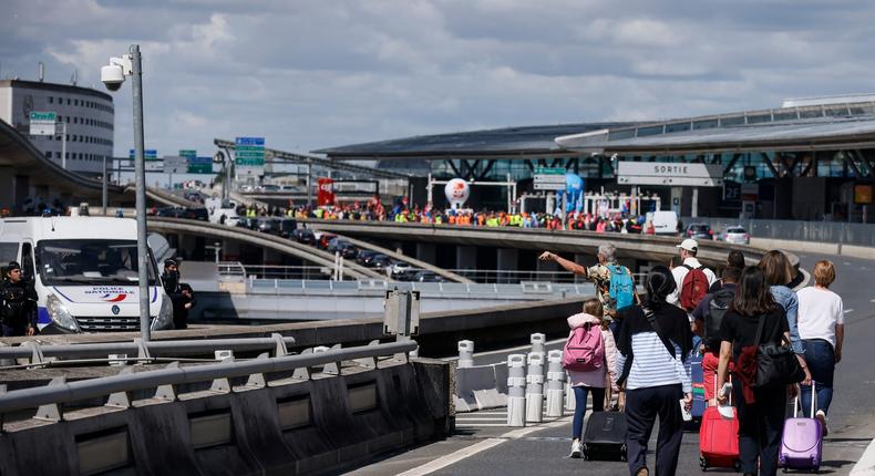 Travelers arrive on foot at Roissy-Charles de Gaulle airport while airport workers demonstrate, Friday, July 1, 2022 at Roissy airport, north of Paris.