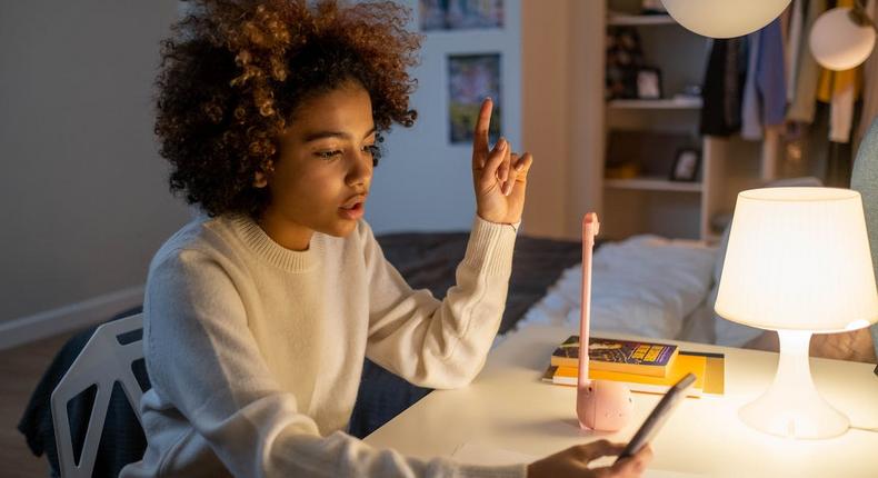 A teenager sitting on a desk while holding a phone [Image Credit: Cottonbro Studio]