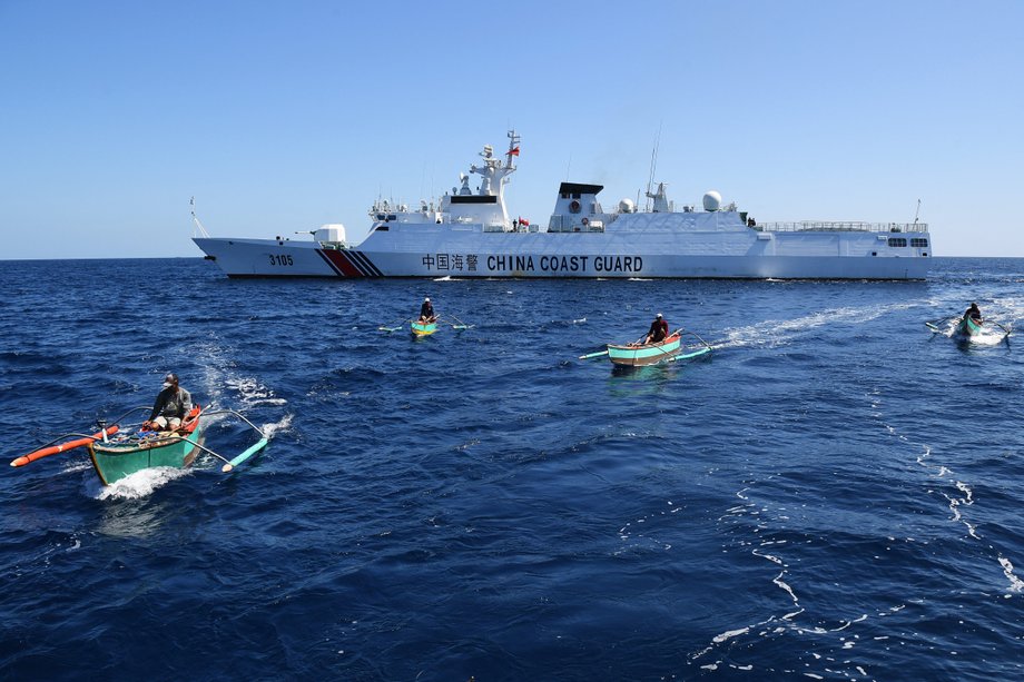 Filipińscy rybacy na pokładzie swoich drewnianych łodzi przepływają obok chińskiego statku straży przybrzeżnej w pobliżu Scarborough Shoal, na spornych wodach Morza Południowochińskiego.