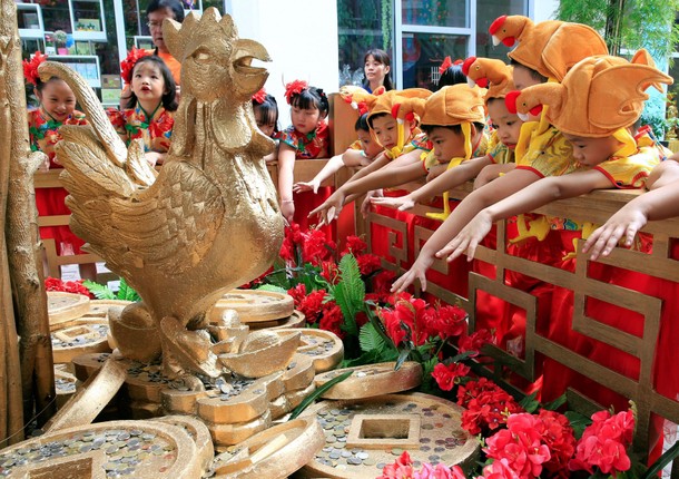 Filipino-Chinese students with rooster hats gesture after tossing a coin in front of a Prosperity Tr