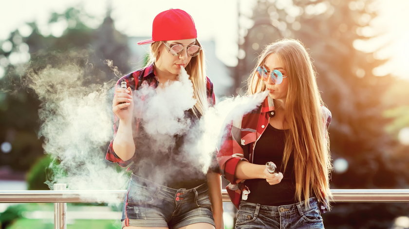 Two women vaping outdoor. The evening sunset over the city. Toned image.