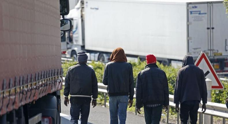 Migrants walk near trucks blocked on a road which leads to the Channel Tunnel terminal in Coquelles near Calais, northern France, July 1, 2015.    REUTERS/Vincent Kessler