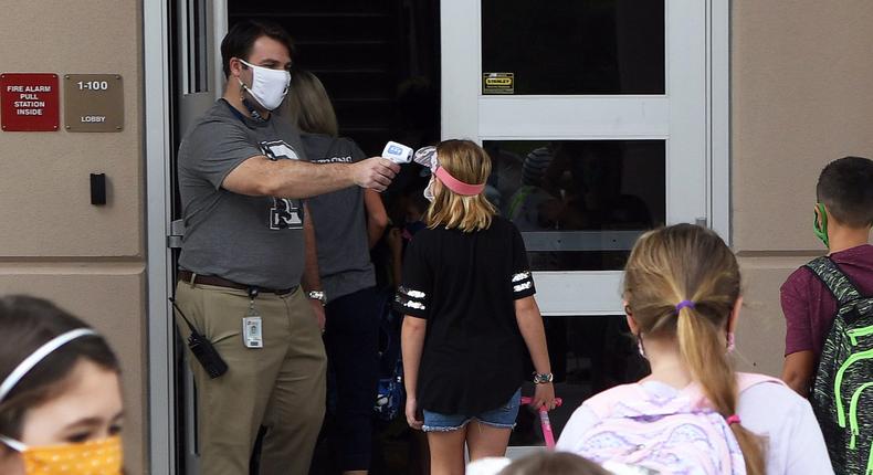 Principal Nathan Hay checks the temperatures of students as they return to school on the first day of in-person classes in Orange County at Baldwin Park Elementary School on August 21, 2020 in Orlando, Florida, US. Face masks and temperature checks are required for all students as Florida's death toll from COVID-19 now exceeds 10,000, with some teachers refusing to return to their classrooms due to health concerns.