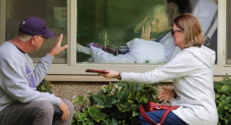 Judie Shape, center, who has tested positive for the coronavirus, blows a kiss to her son-in-law, Michael Spencer, left, as Shape's daughter, Lori Spencer, right, looks on, Wednesday, March 11, 2020, as they visit on the phone and look at each other through a window at the Life Care Center in Kirkland, Wash., near Seattle.
