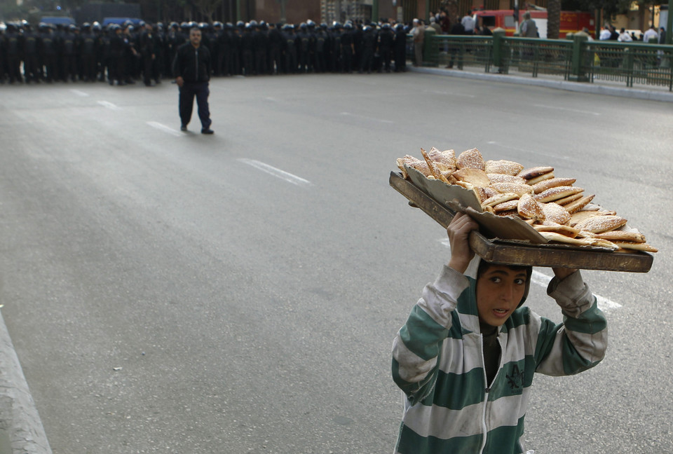 A boy carrying bread on his head runs away from a column of riot policeman during anti-government protests in downtown Cairo