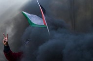 Protester holds a Palestinian flag as smoke rises from a burning tyre during clashes with Israeli tr