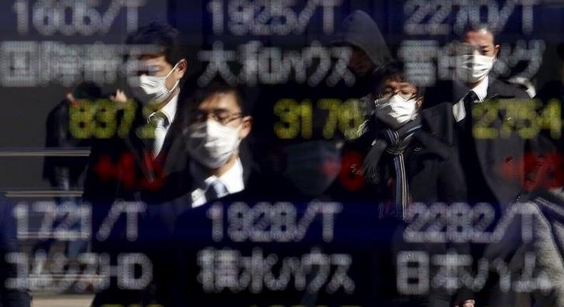 Pedestrians wearing masks are reflected in an electronic board showing various stock prices outside a brokerage in Tokyo, Japan, February 26, 2016. 