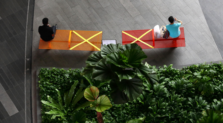 Egy szingapúri bevásárlóközpontban részlegesen lezárt padokon ülő emberek 2020. április 2-án