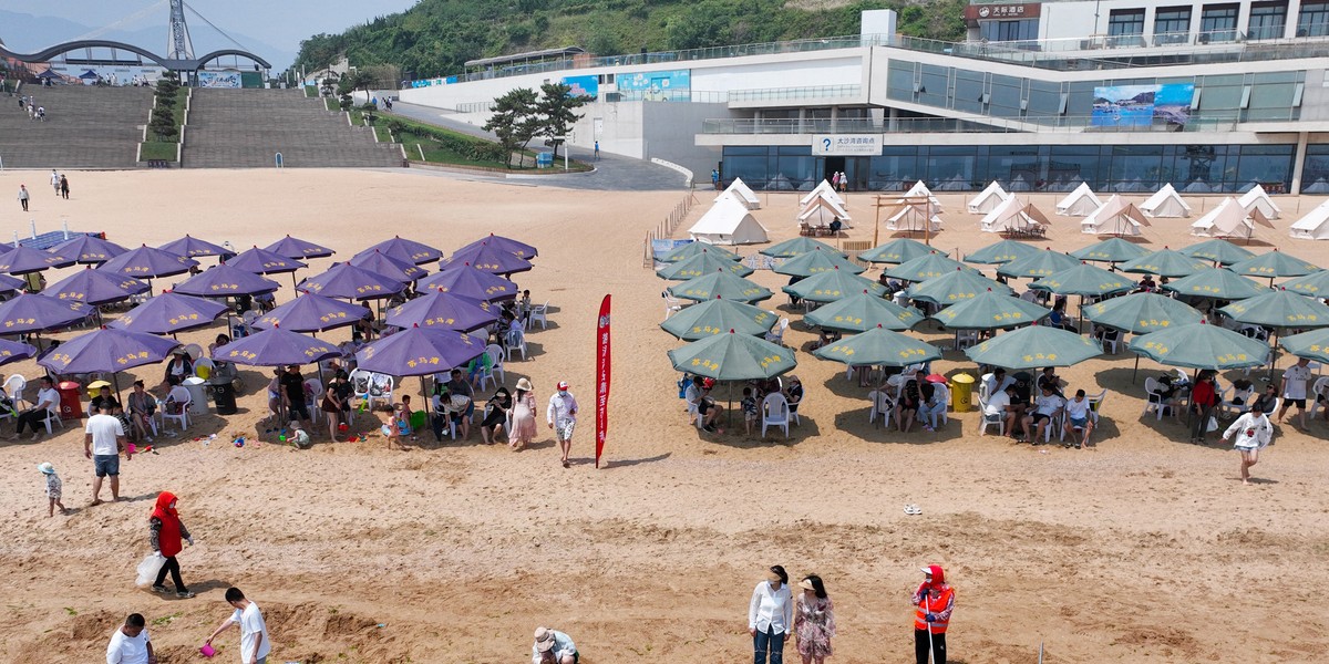 Turyści uciekający przed letnim upałem pod parasolami na plaży Liandao w chińskiej prowincji Jiangsu. 18 czerwca 2022 r. 