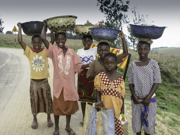 Uśmiechnięta grupa młodych mieszkańców wsi niesie w koszach zboże niedaleko hodowli bydła na ranczu Obudu. Pobliże granicy z Kamerunem. Obudu, Nigeria 2004