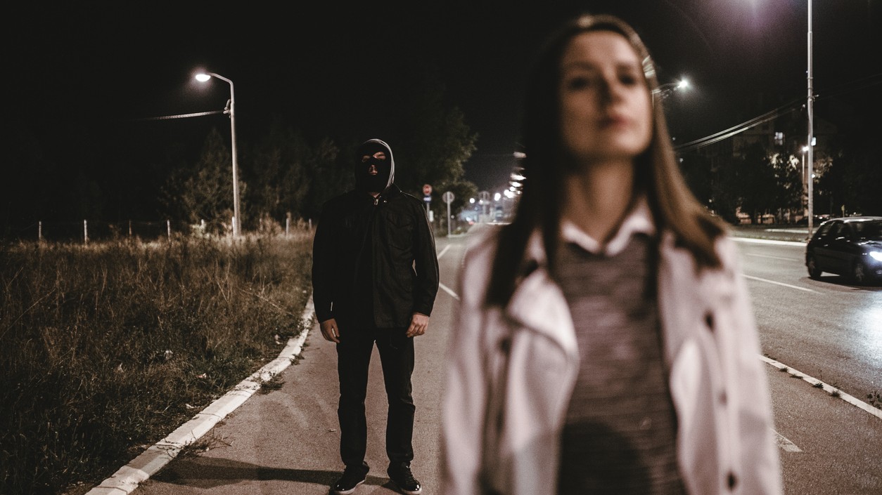 Žena kráča osamote ulicou, zatiaľ čo v pozadí stojí neznámy muž. Pocit, že nás niekto sleduje, môže vzniknúť aj na základe nenápadných podnetov, ktoré mozog vyhodnotí ako možnú prítomnosť iného človeka. Niekedy však môže ísť iba o mylný dojem. (Ilustračný obrázok)