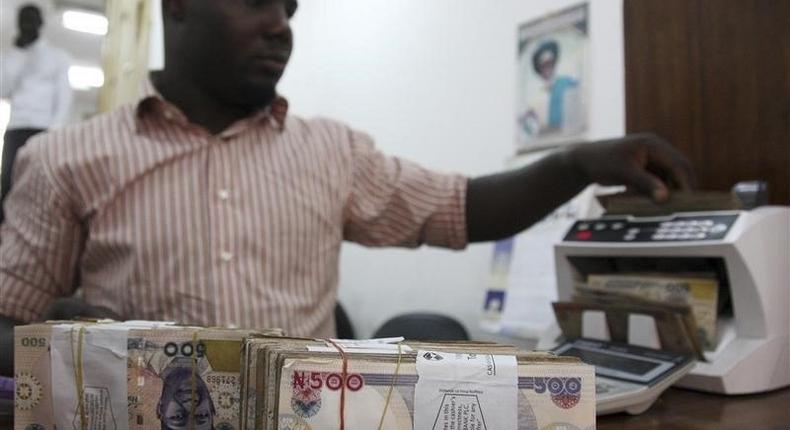 A money dealer counts the Nigerian naira on a machine in his office in the commercial capital of Lagos, file. REUTERS/Akintunde Akinleye
