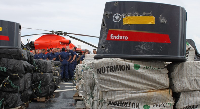 The crew of the Coast Guard cutter James stands behind bales of cocaine with disabled engine cowlings stacked on them in Ft. Lauderdale, Florida, November 15, 2018.