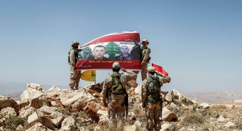 Hezbollah fighters giving a guided tour near the Lebanese-Syrian border on July 26, 2017 raise a Lebanese flag showing pictures of soldiers killed fighting jihadists