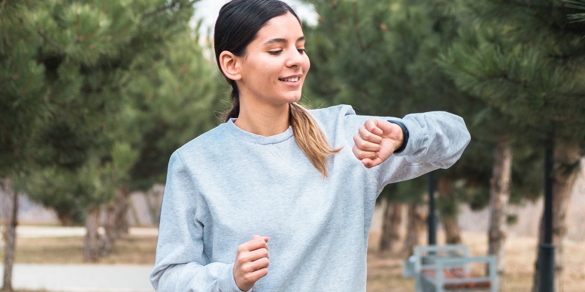 cheerful woman checking her smartband after morning run in park. girl checking burned calories after