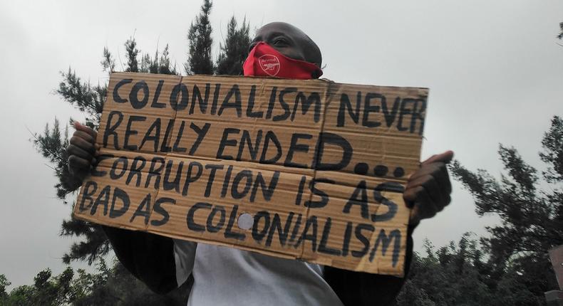 Protester holding placard in Nairobi which reads: Colonialism never really ended. Corruption is as bad as colonialism.  