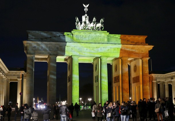 People stand in front of the Brandenburg gate, which is illuminated in the colours of the Belgian fl