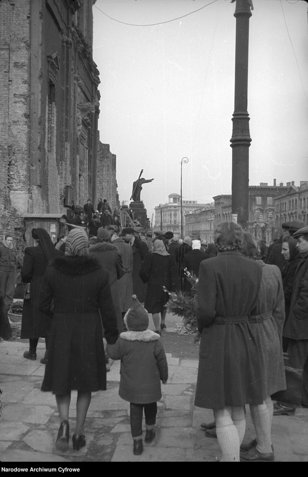 Grupa osób z palmami wielkanocnymi w drodze do kościoła św. Krzyża. W tle z prawej fragment d. Szpitala św. Rocha przy ul. Krakowskie Przedmieście 24, Warszawa, 1947 r.
