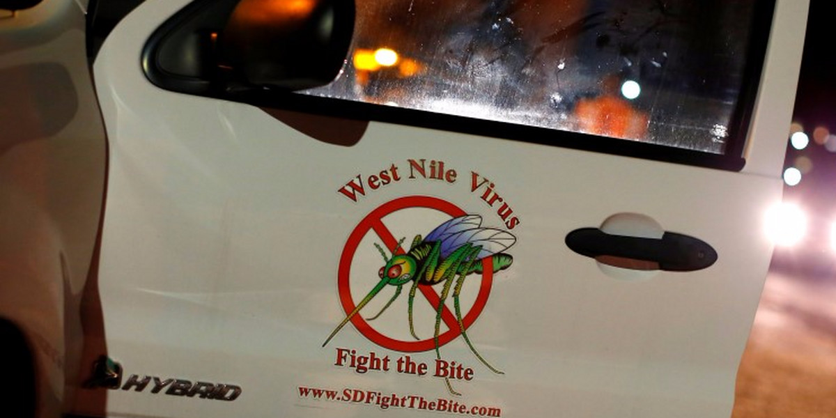A vector control team vehicle displays a sign warning of West Nile Virus before the early morning spraying of a neighborhood.