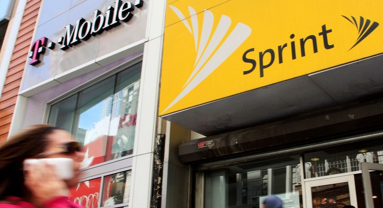 FILE - In this April 27, 2010 file photo, a woman using a cell phone walks past T-Mobile and Sprint stores in New York. T-Mobile, in its attempt to buy Sprint for $26.5 billion, shrinking the major wireless companies to three from four and creating another phone giant to rival AT&T and Verizon, has already notched approvals from federal national-security, telecommunications and antitrust regulators. Now it must convince a federal court judge in New York that the 14 state attorneys general suing to stop its deal are wrong. (AP Photo/Mark Lennihan, File)