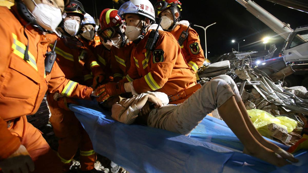 Rescue workers wearing face masks move a boy from the rubble of a collapsed hotel which has been used for medical observation following an outbreak of the novel coronavirus, in the southeast Chinese port city of Quanzhou, Fujian